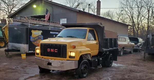 Yellow GMC dump truck parked in front of a building, next to a trailer.