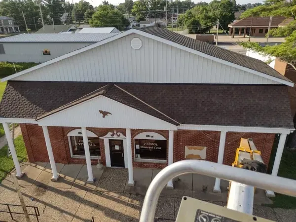 Brick building with white trim and brown roof. Columns support a front porch, with windows and a doorway.