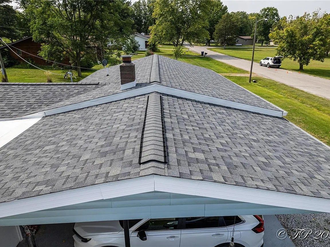 Overhead view of a roof with gray shingles, a carport, and a street with houses.