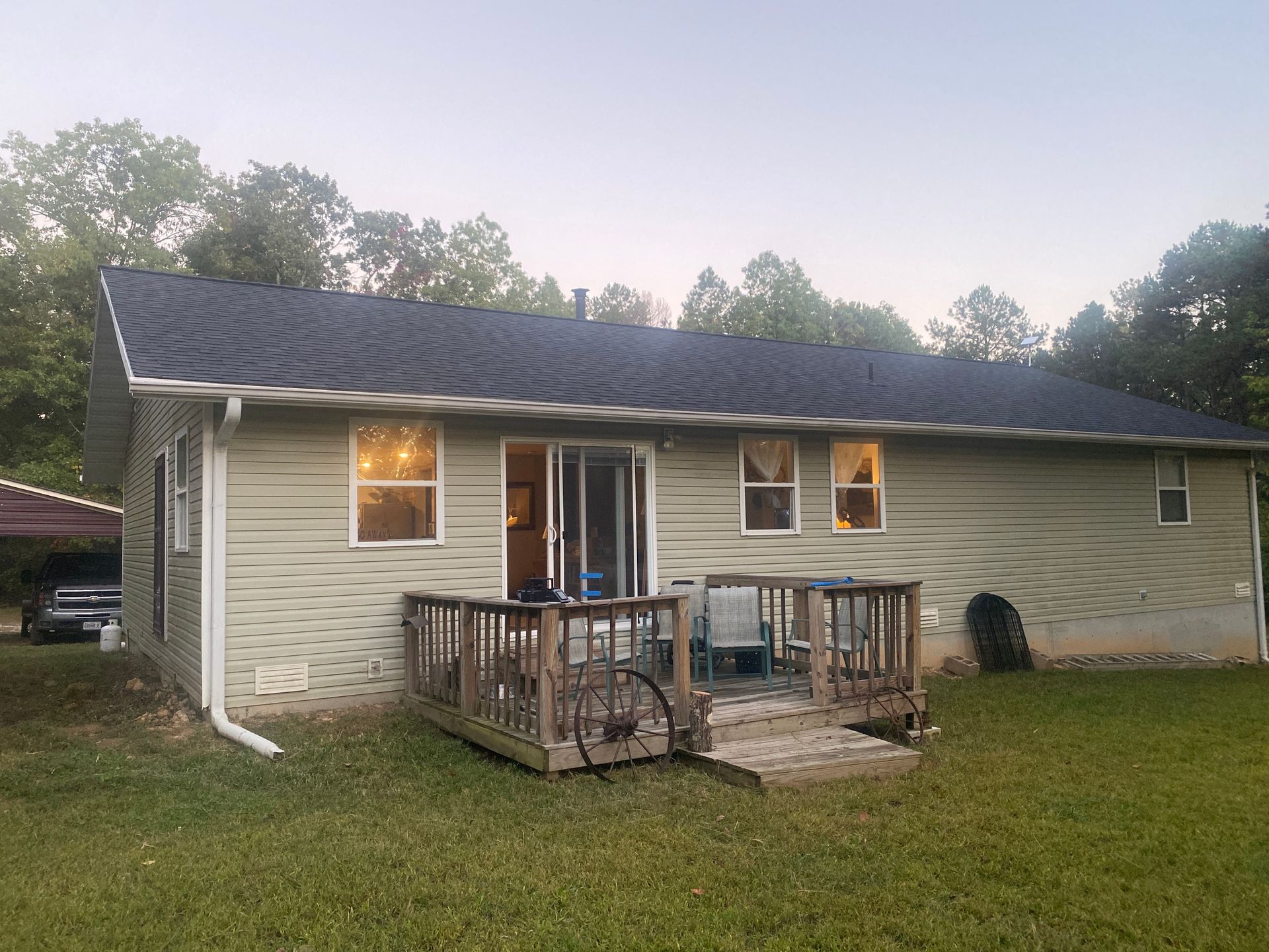 Back view of a house with a deck and siding, dusk setting.