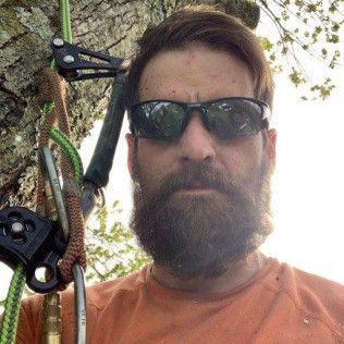 A man with a beard and sunglasses is hanging from a tree.