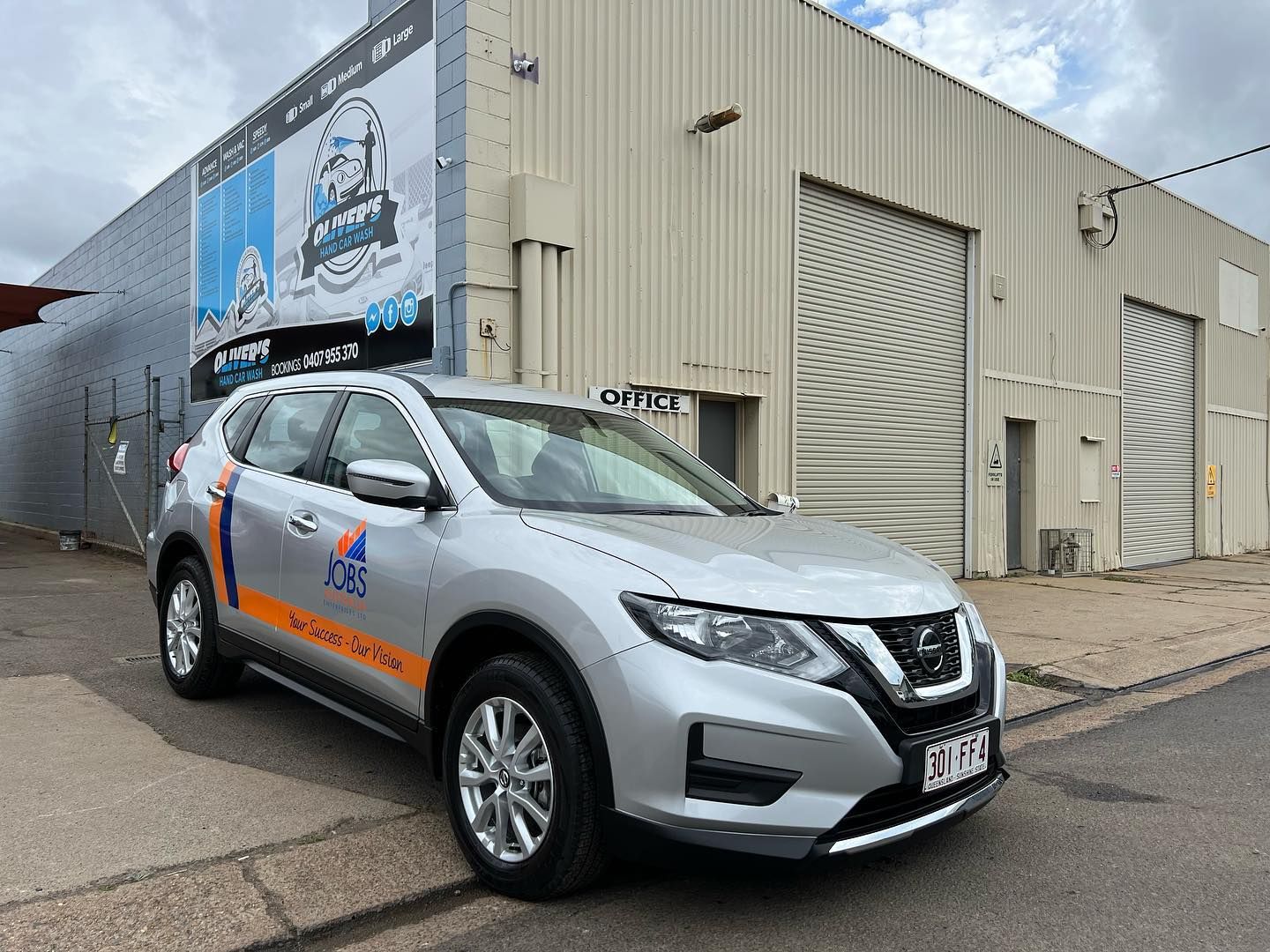 A white and yellow pickup truck with company logos parked in front of a building with a large sign. 