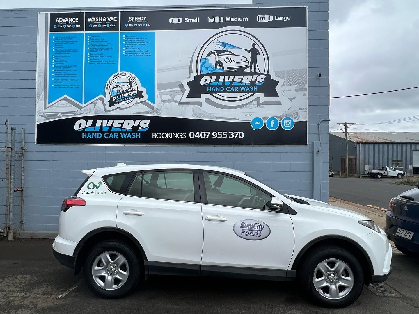 White SUV parked in front of Oliver's Hand Car Wash sign. The building is grey, and the sky is overcast. — Oliver's Hand Car Wash in Norville, QLD