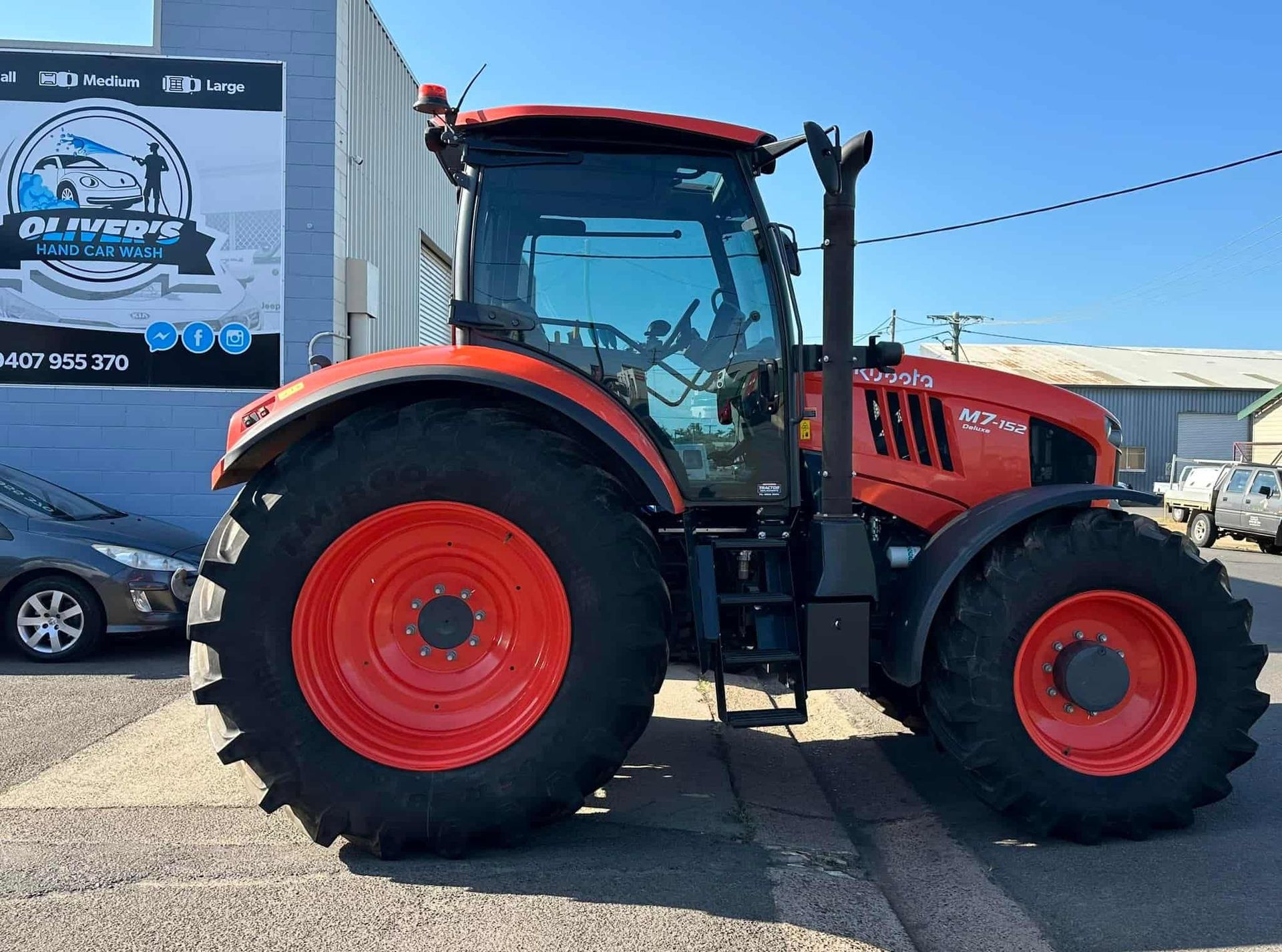Red Kubota tractor parked next to a building on a sunny day. — Oliver's Hand Car Wash in Norville, QLD