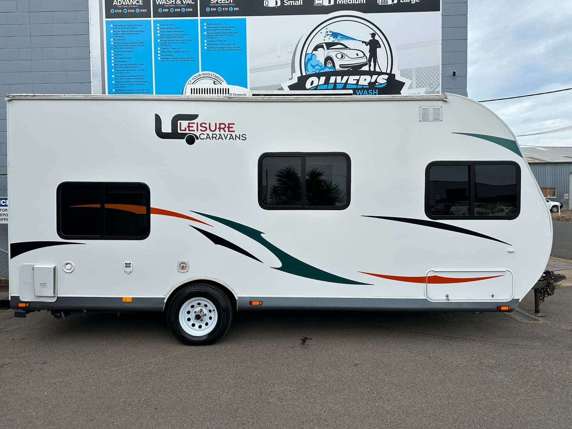 White camper trailer with curved front, black windows, and decorative green and orange stripes. — Oliver's Hand Car Wash in Norville, QLD