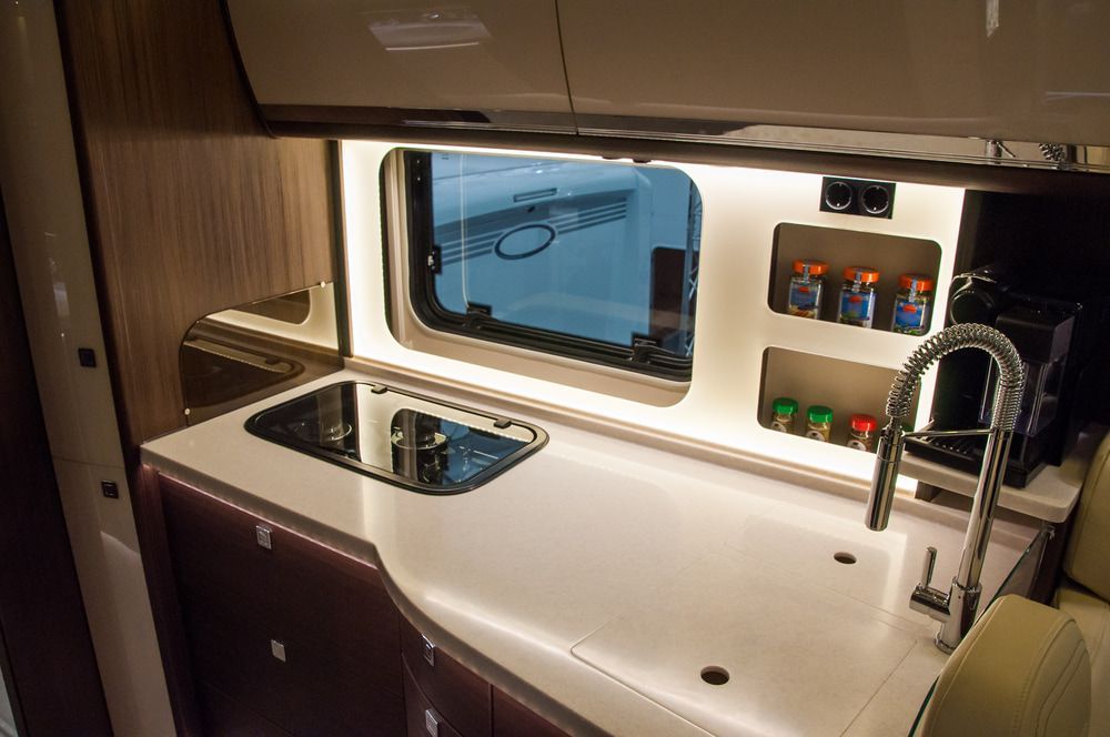 RV kitchen interior with a stovetop, sink, window, and storage shelves. — Oliver's Hand Car Wash in Norville, QLD