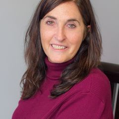 Woman with dark hair in a burgundy turtleneck smiles at the camera.
