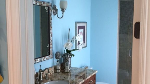 A bathroom with blue walls , a sink , a mirror and a toilet.