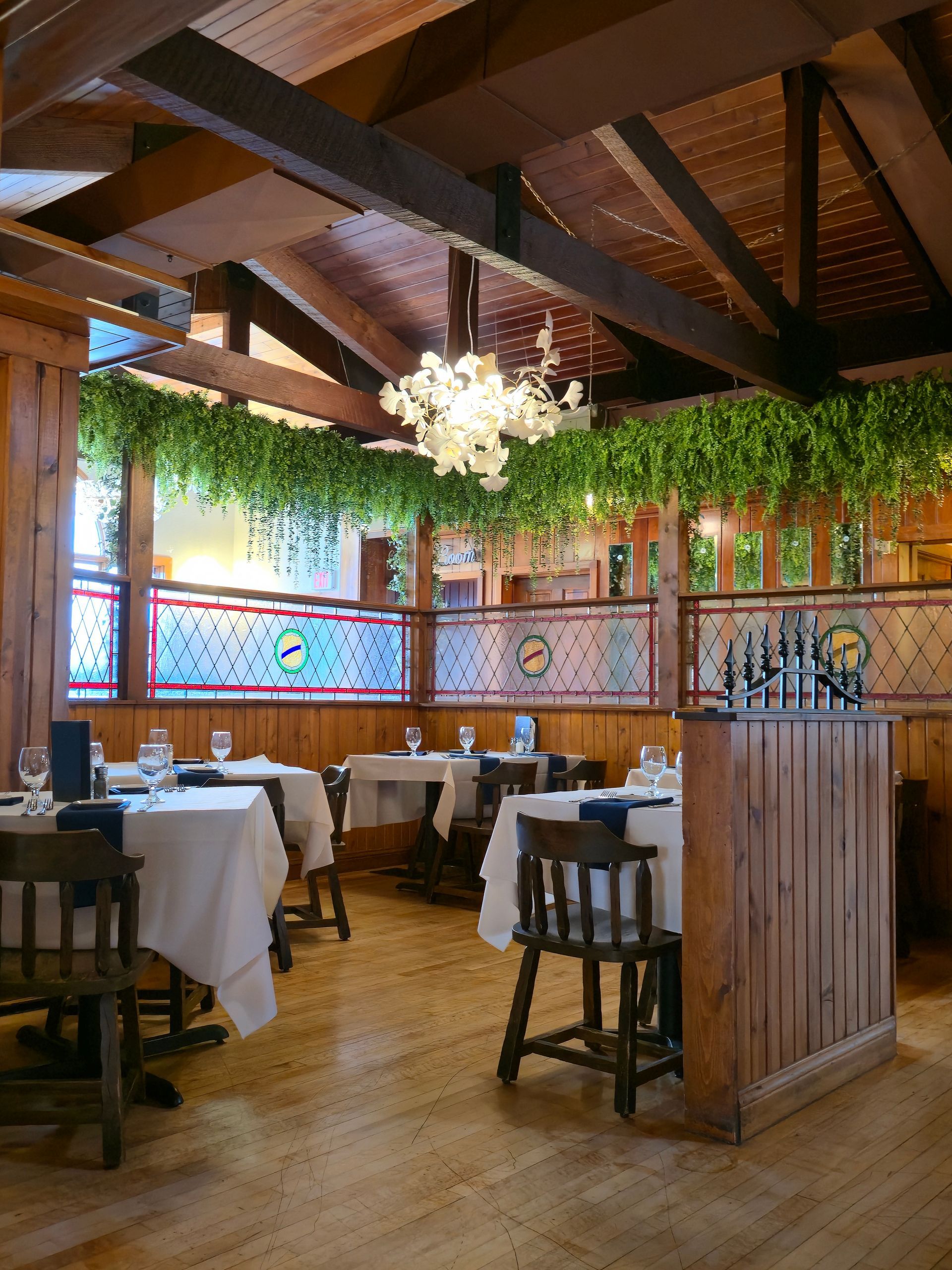 Elegant dining room, tables set with white linens, crystal chandelier hanging from a wooden ceiling.
