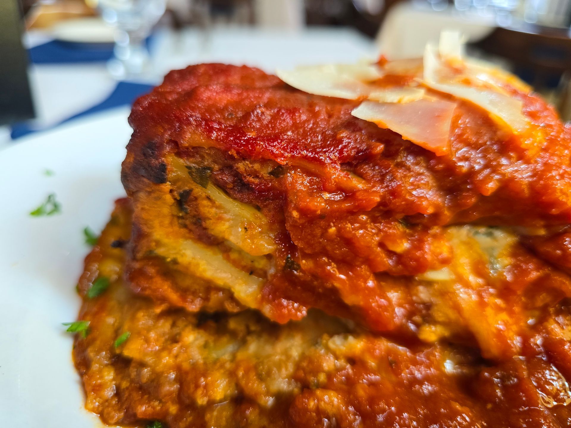 A thick slice of eggplant parmigiana layered with rich tomato sauce and topped with shaved parmesan on a white plate.