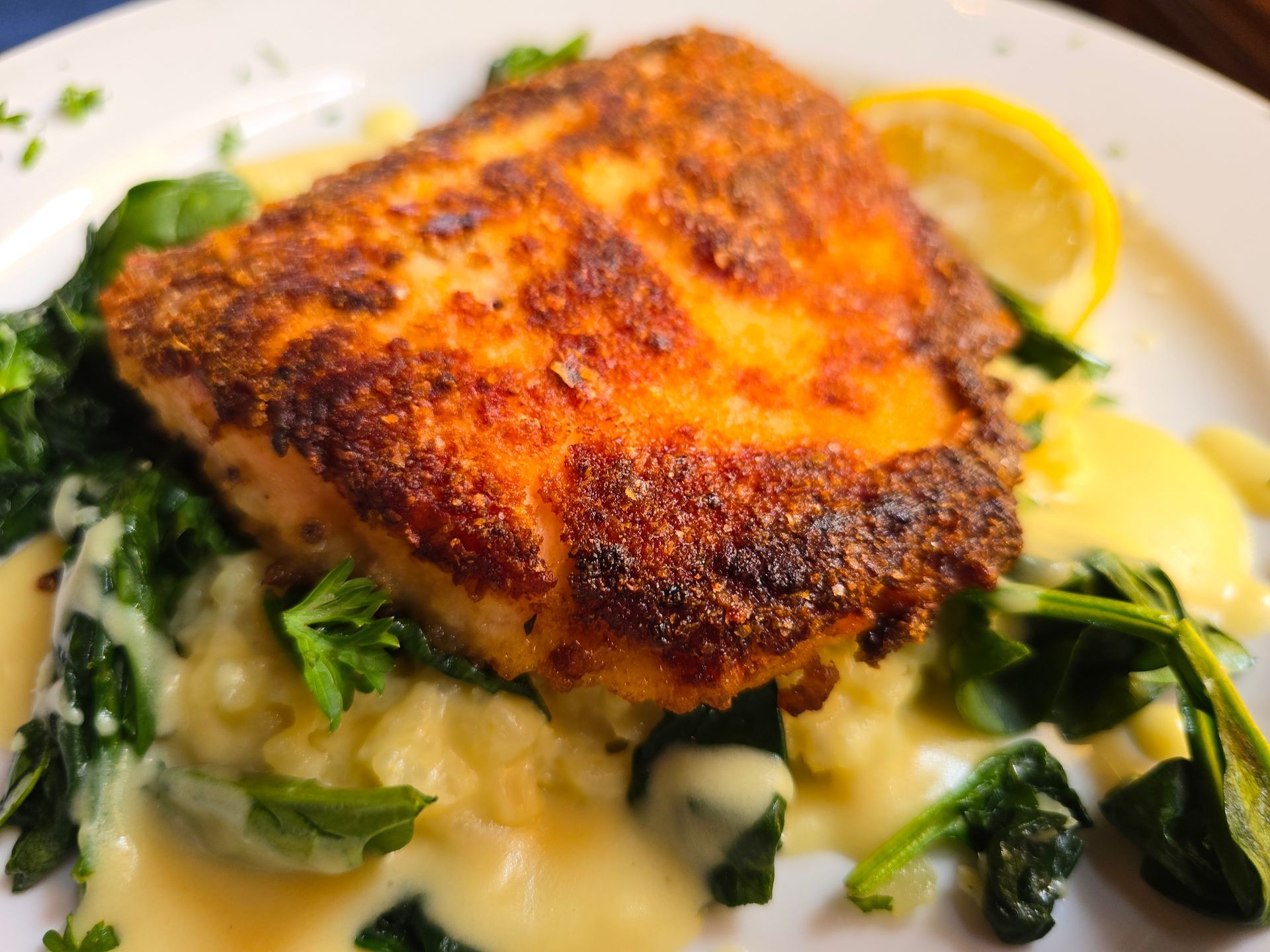 A golden-brown pan-seared fish fillet served on a bed of sautéed spinach and mashed potatoes with a creamy sauce.