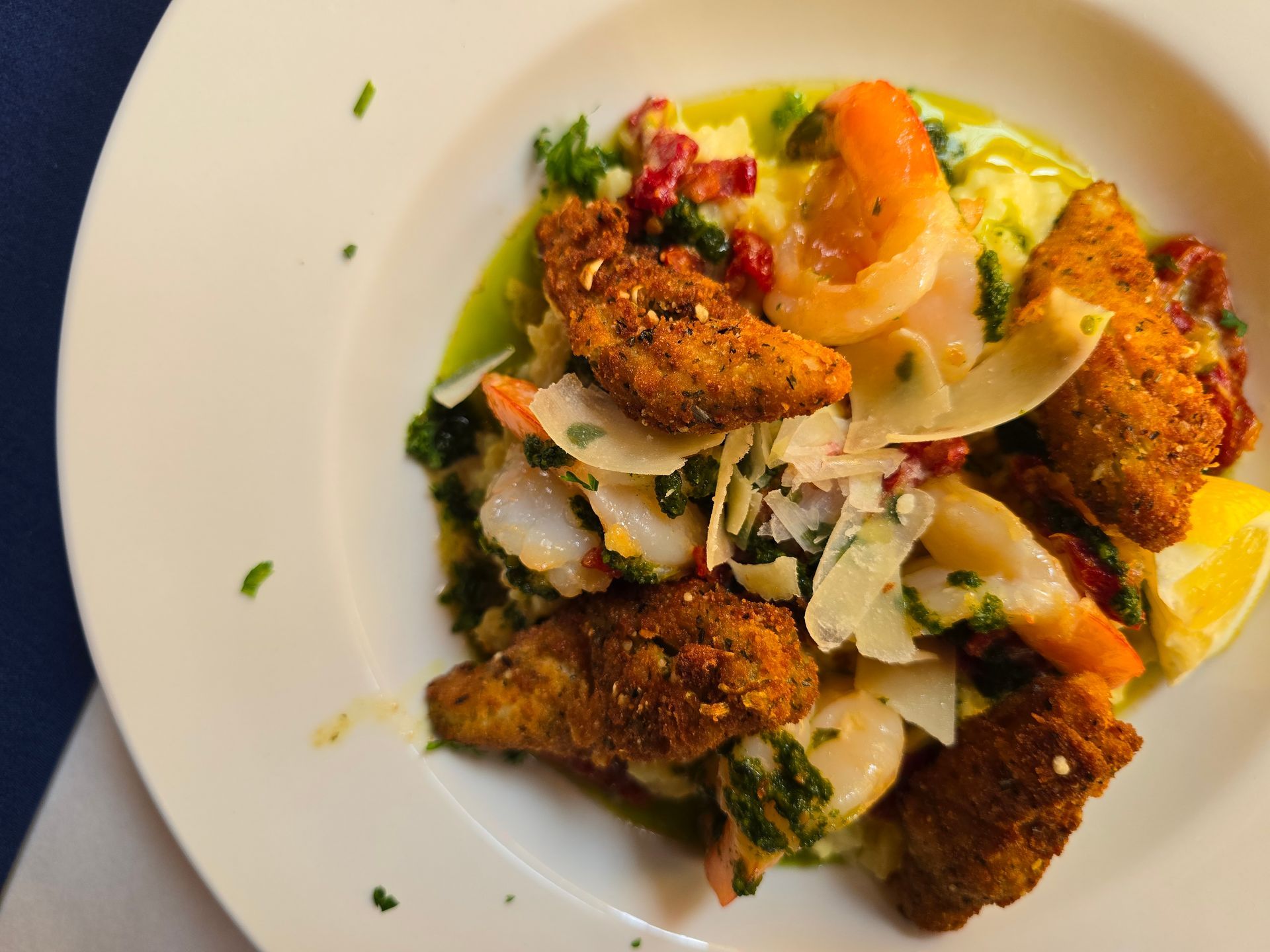 A bowl of crispy fried seafood served over polenta with shaved cheese, herbs, and a lemon wedge.