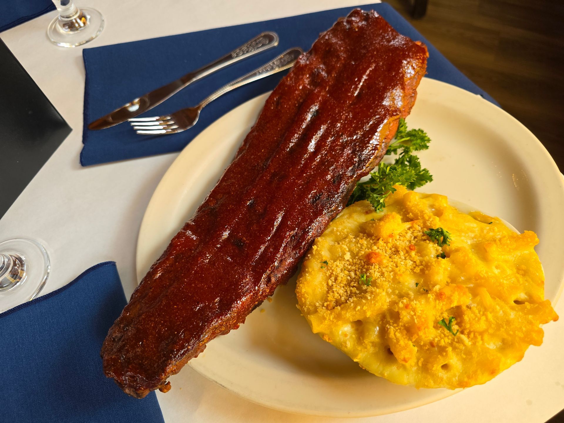 A rack of glazed ribs next to a serving of macaroni and cheese on a white plate, set on a table with blue napkins.