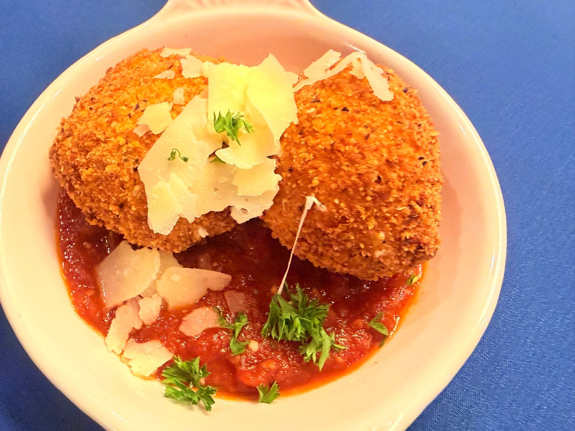Two breaded, fried cheese balls atop tomato sauce, garnished with parsley and parmesan, in a white dish.