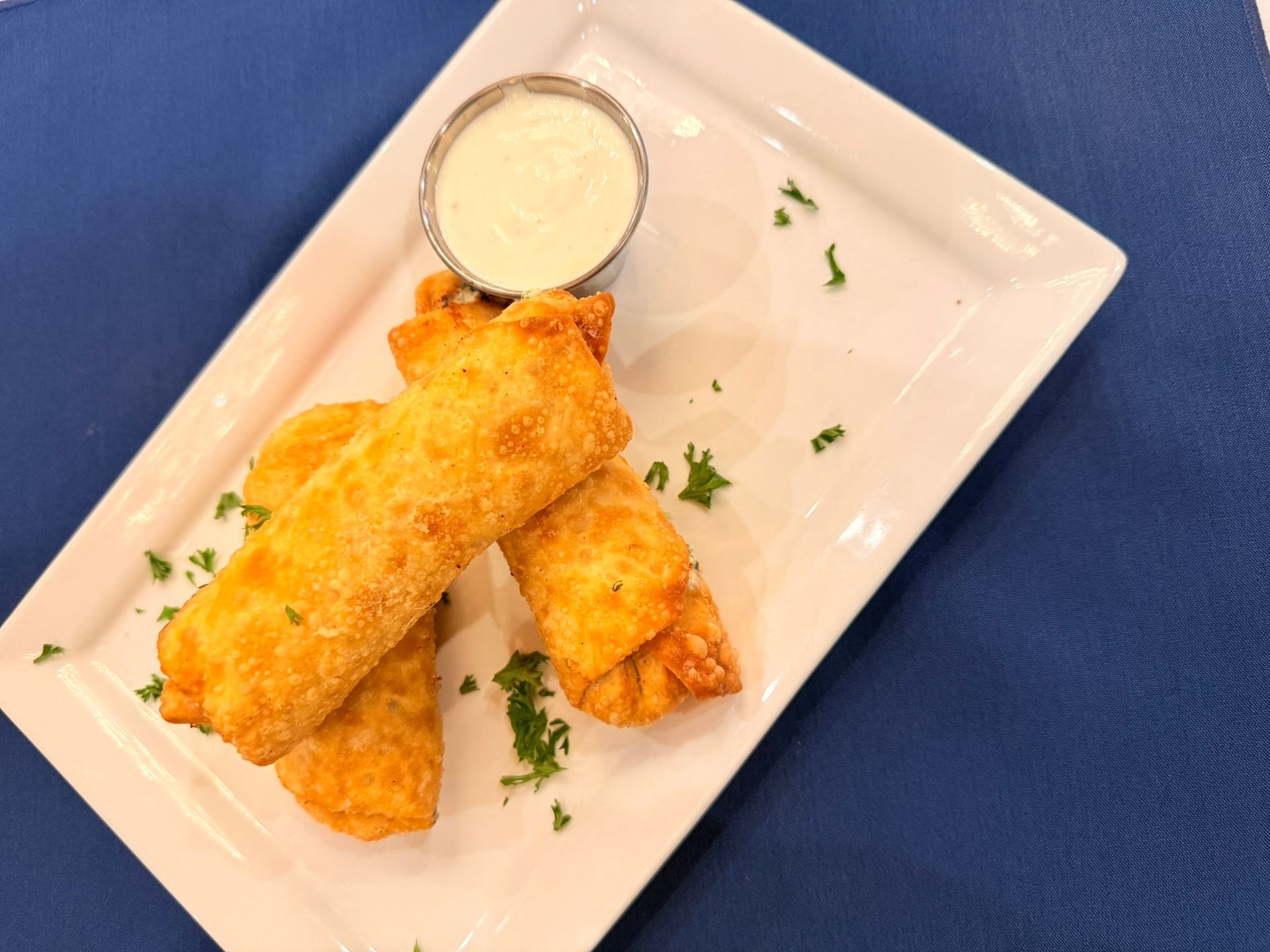 Fried egg rolls with dipping sauce on a white plate, blue background.