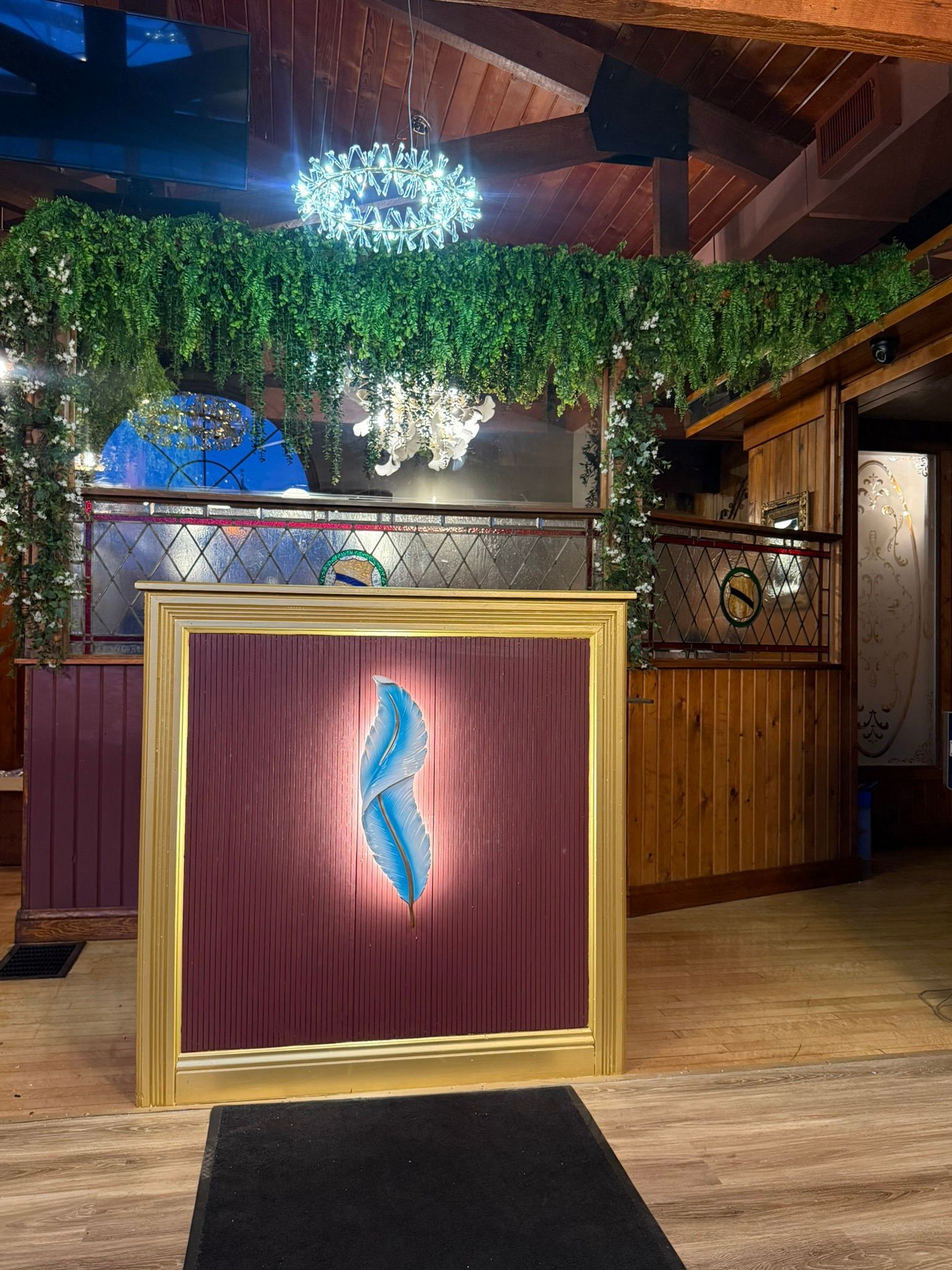 Artwork with a gold frame and blue design stands in front of a decorative restaurant entrance, covered with greenery.