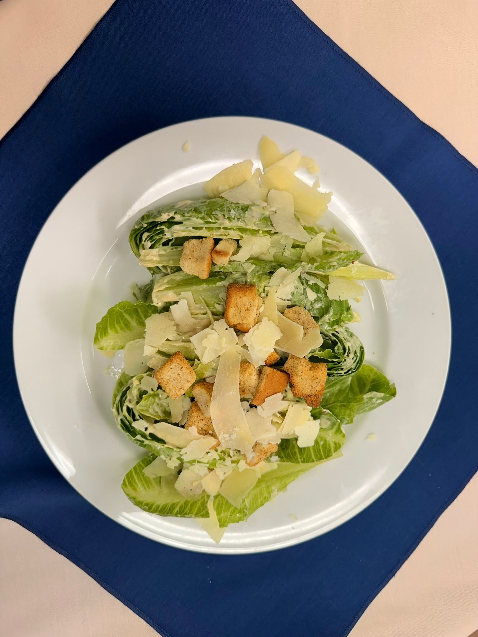 Caesar salad on a white plate: romaine lettuce, croutons, parmesan cheese, creamy dressing.