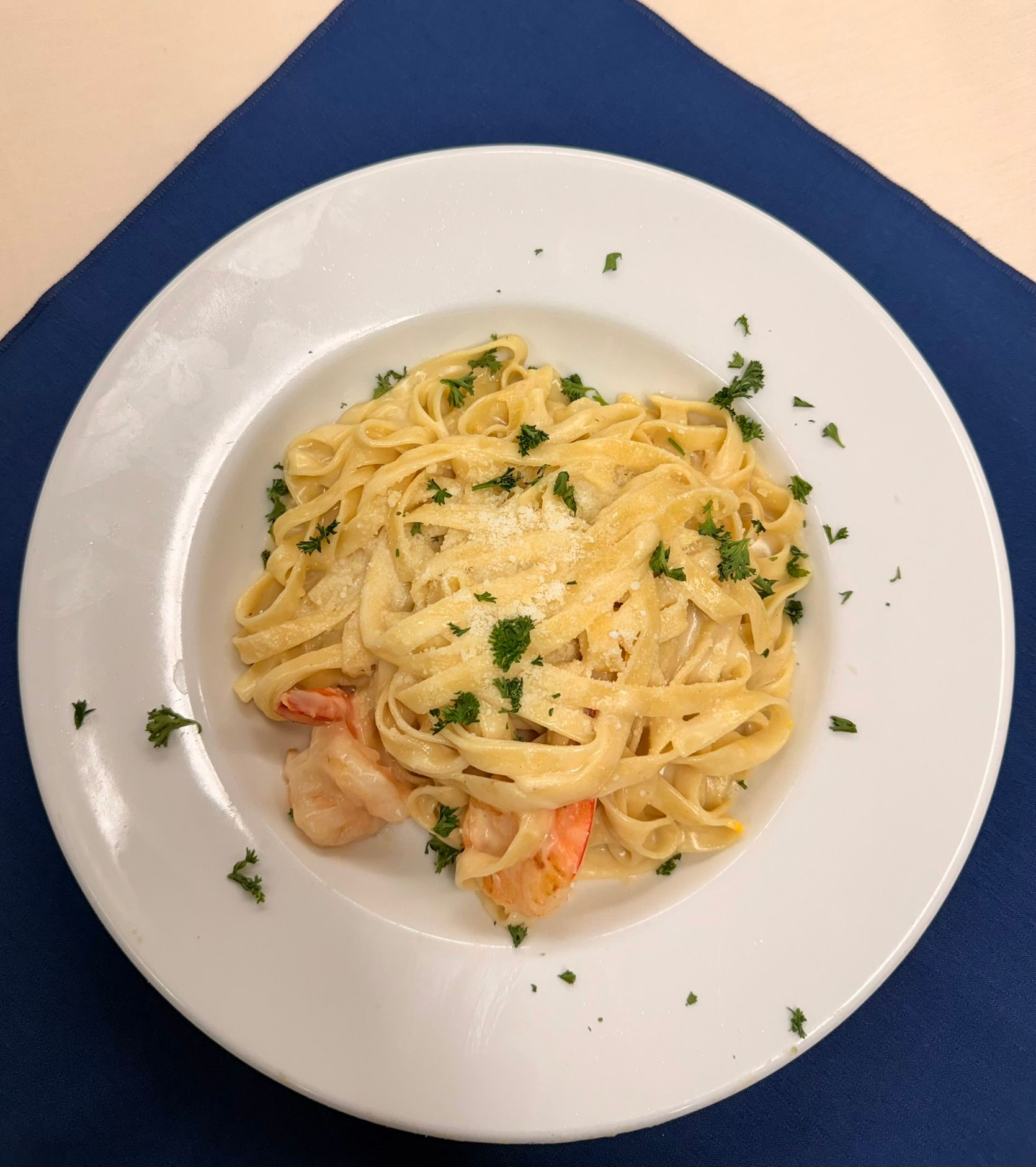 Fettuccine Alfredo with shrimp on a white plate, garnished with parsley on a blue tablecloth.