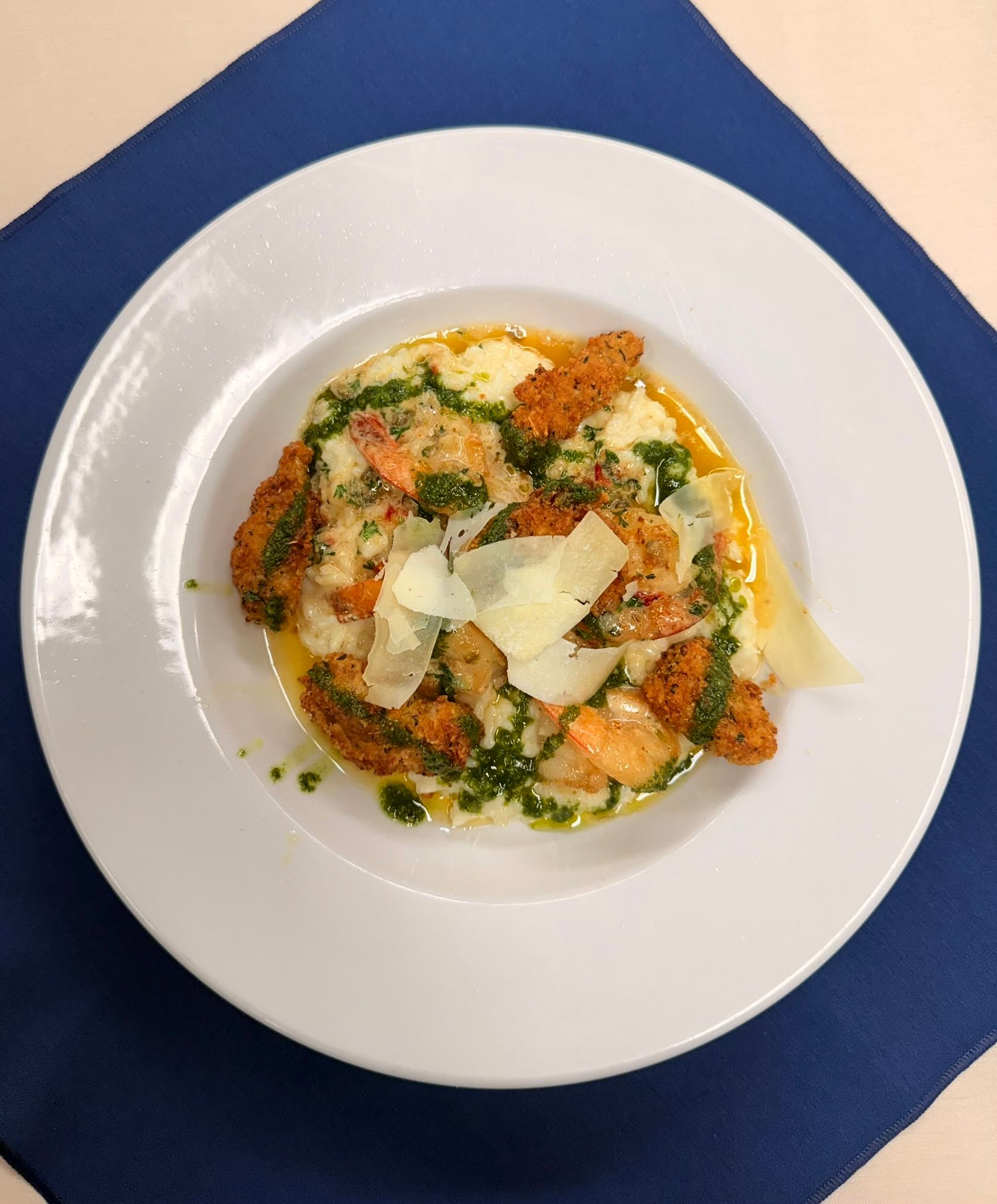 Creamy risotto topped with breaded shrimp, pesto, and Parmesan cheese, served on a white plate.