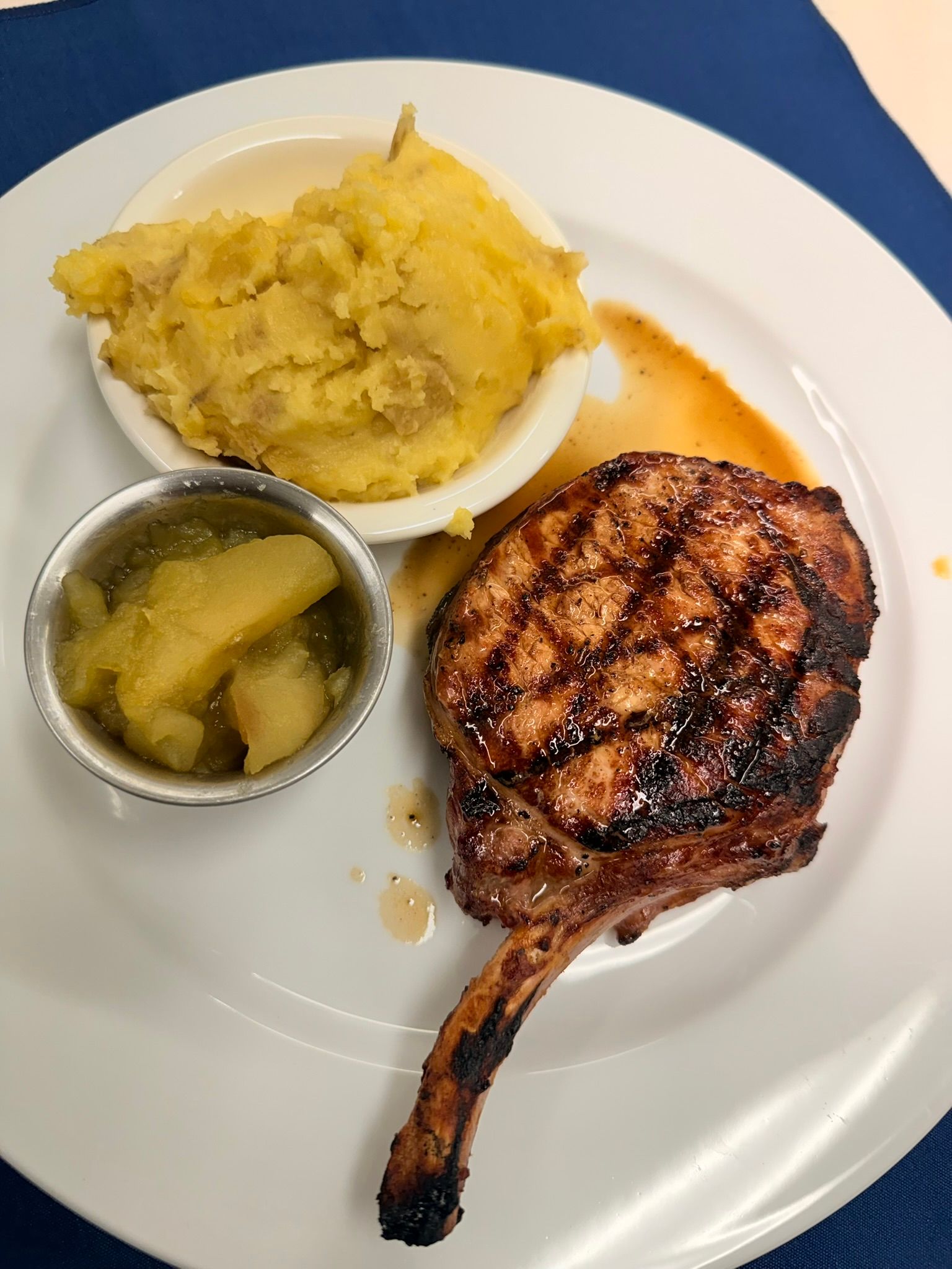 Grilled pork chop with mashed potatoes and applesauce on a white plate.