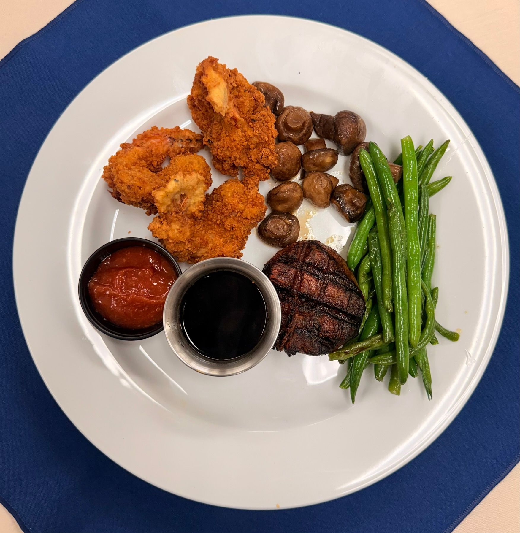 Plate with fried shrimp, steak, mushrooms, green beans, and dipping sauces.