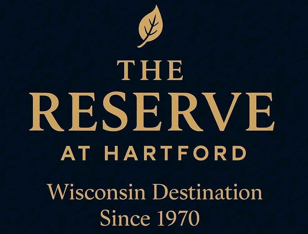 Logo for The Reserve at Hartford, a Wisconsin destination, with text in gold on a navy background. Includes a leaf icon.