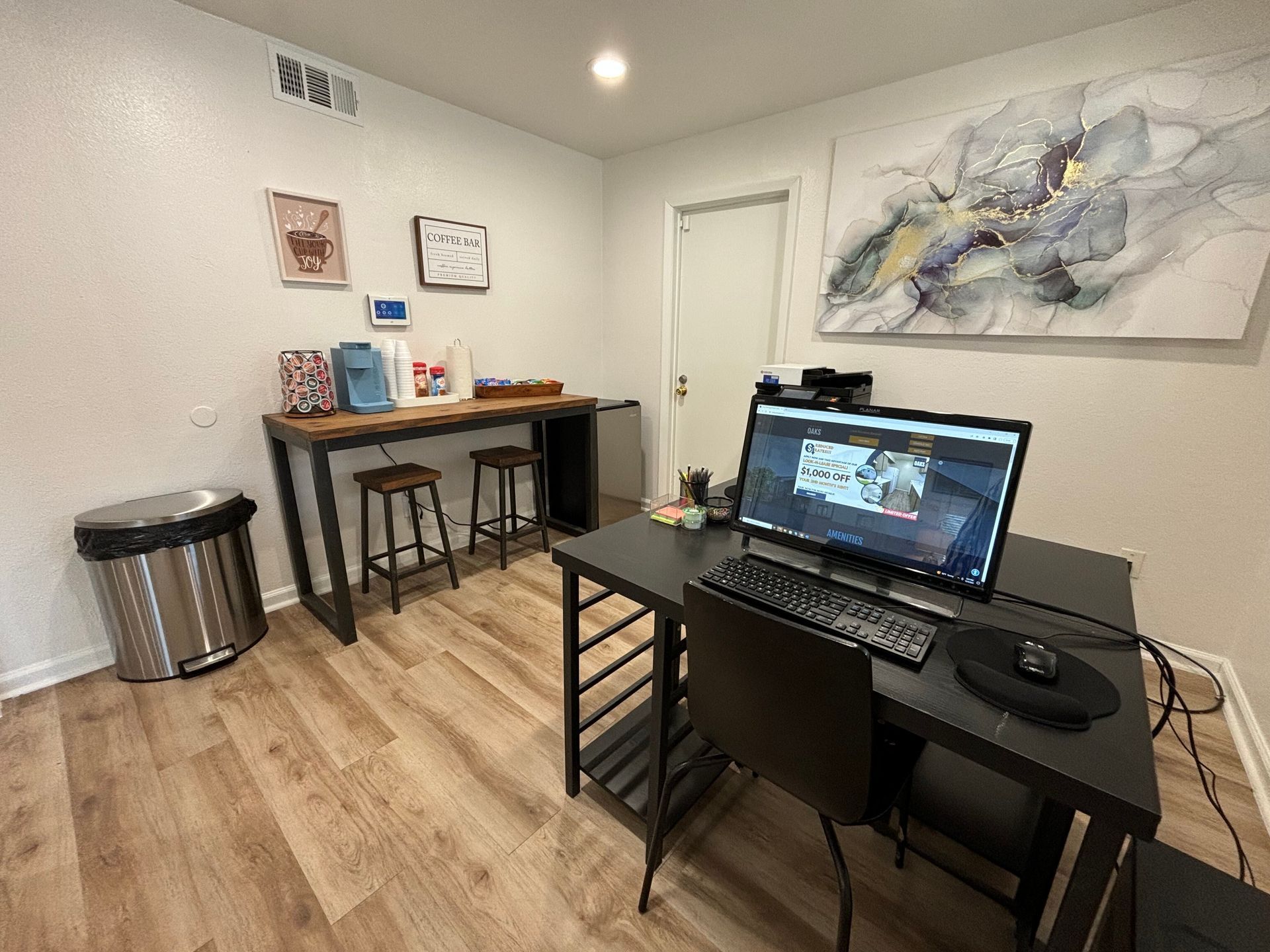A room with a desk , chair , computer and trash can.