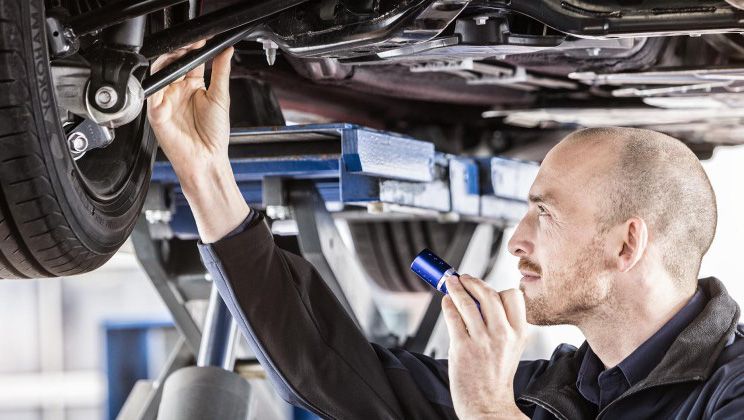 a man is examining the underside of a car with a flashlight .