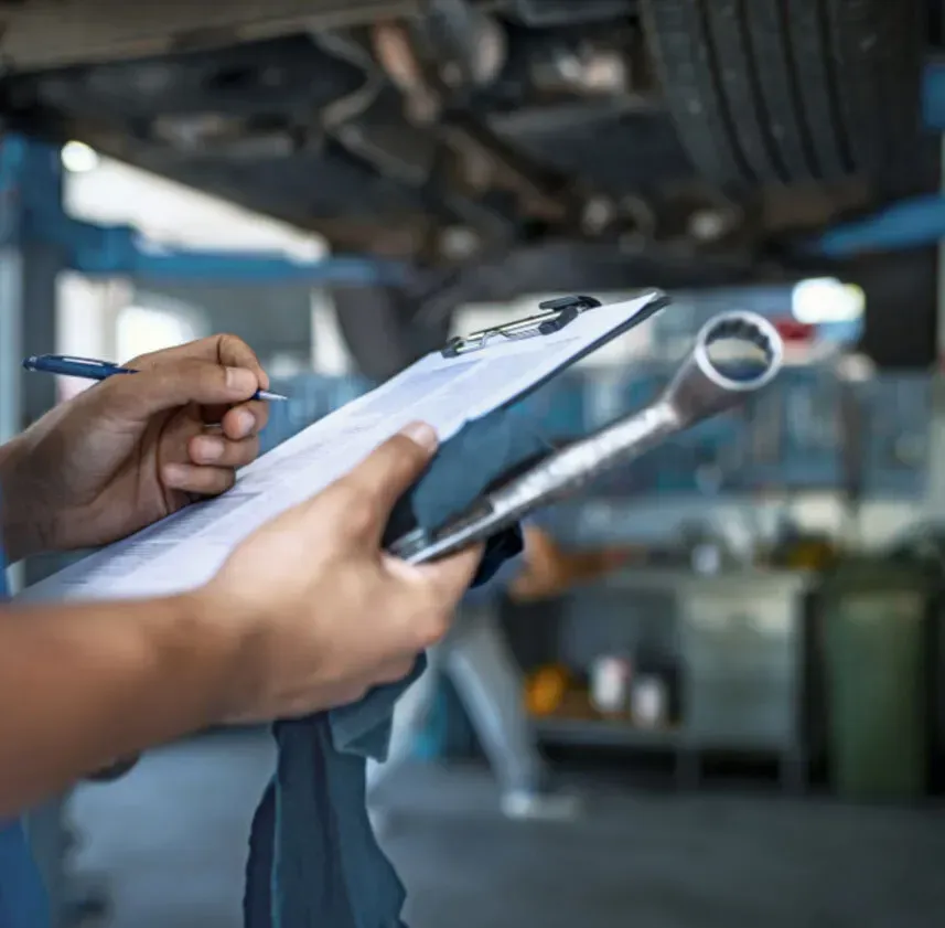 a person is holding a clipboard and a wrench in a garage .
