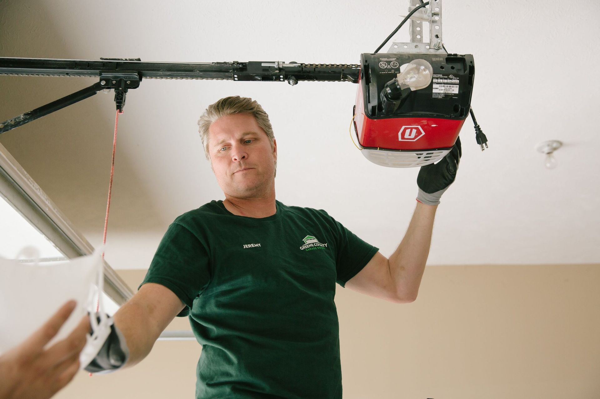 A man in a green shirt is fixing a garage door opener.