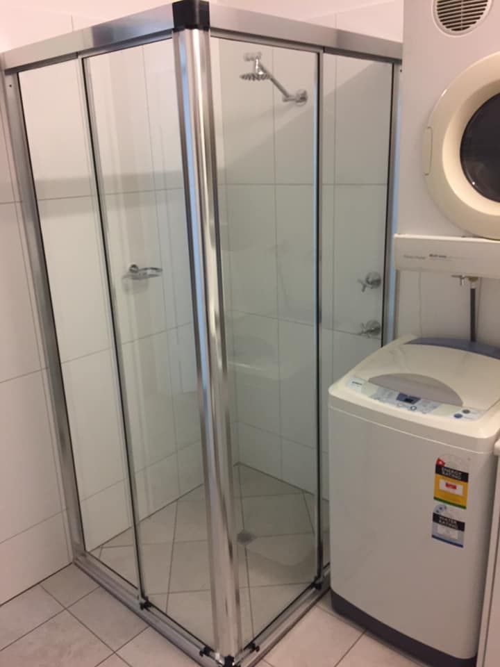 Shower Stall With Sliding Glass Doors Next To A Washing Machine And Dryer