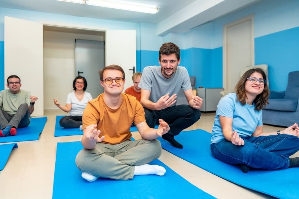 A Group of Six People Sit on Blue Yoga Mats in a Bright Room