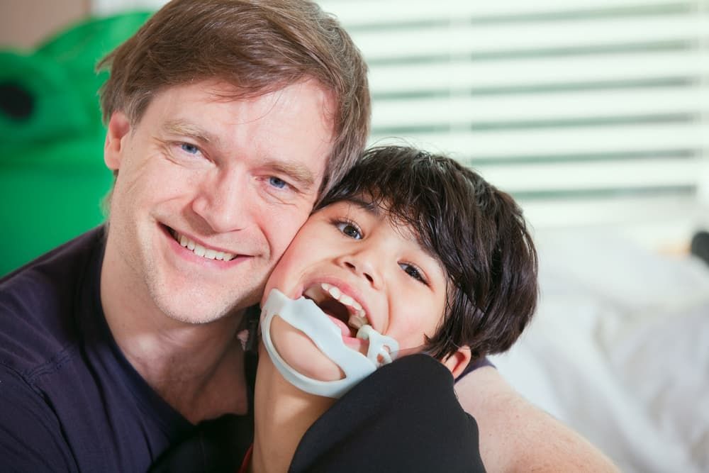 A Smiling Man Embraces a Young Boy Wearing a Protective Chin Strap