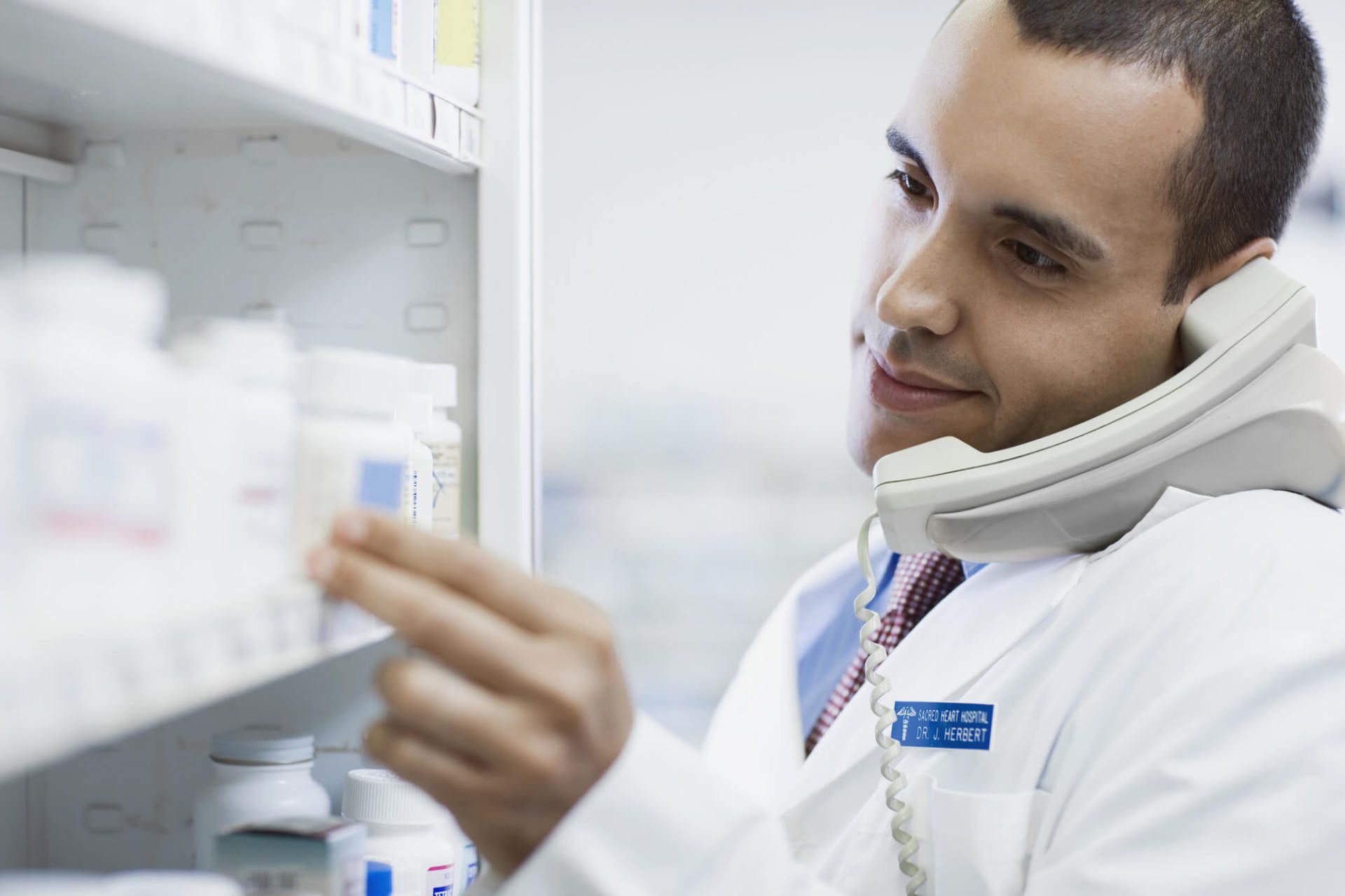 Smiling pharmacist listen to someone on the phone whilst picking out medication