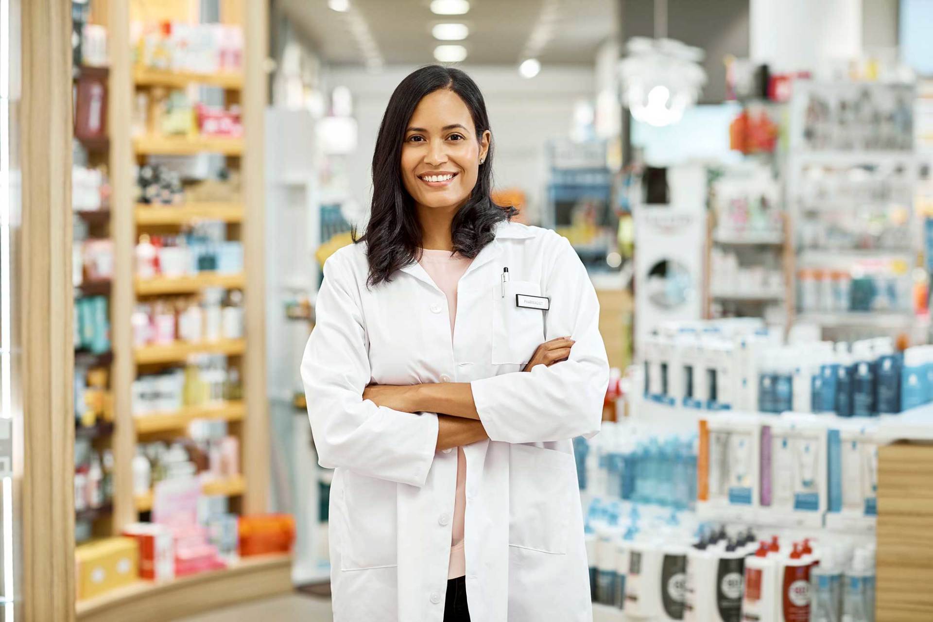 Smiling pharmacist with shelves on medication in the background