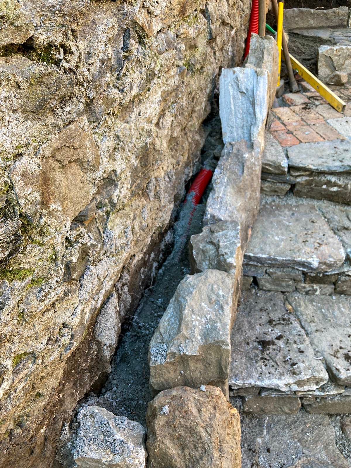 Un muro di pietra da cui esce un tubo rosso.