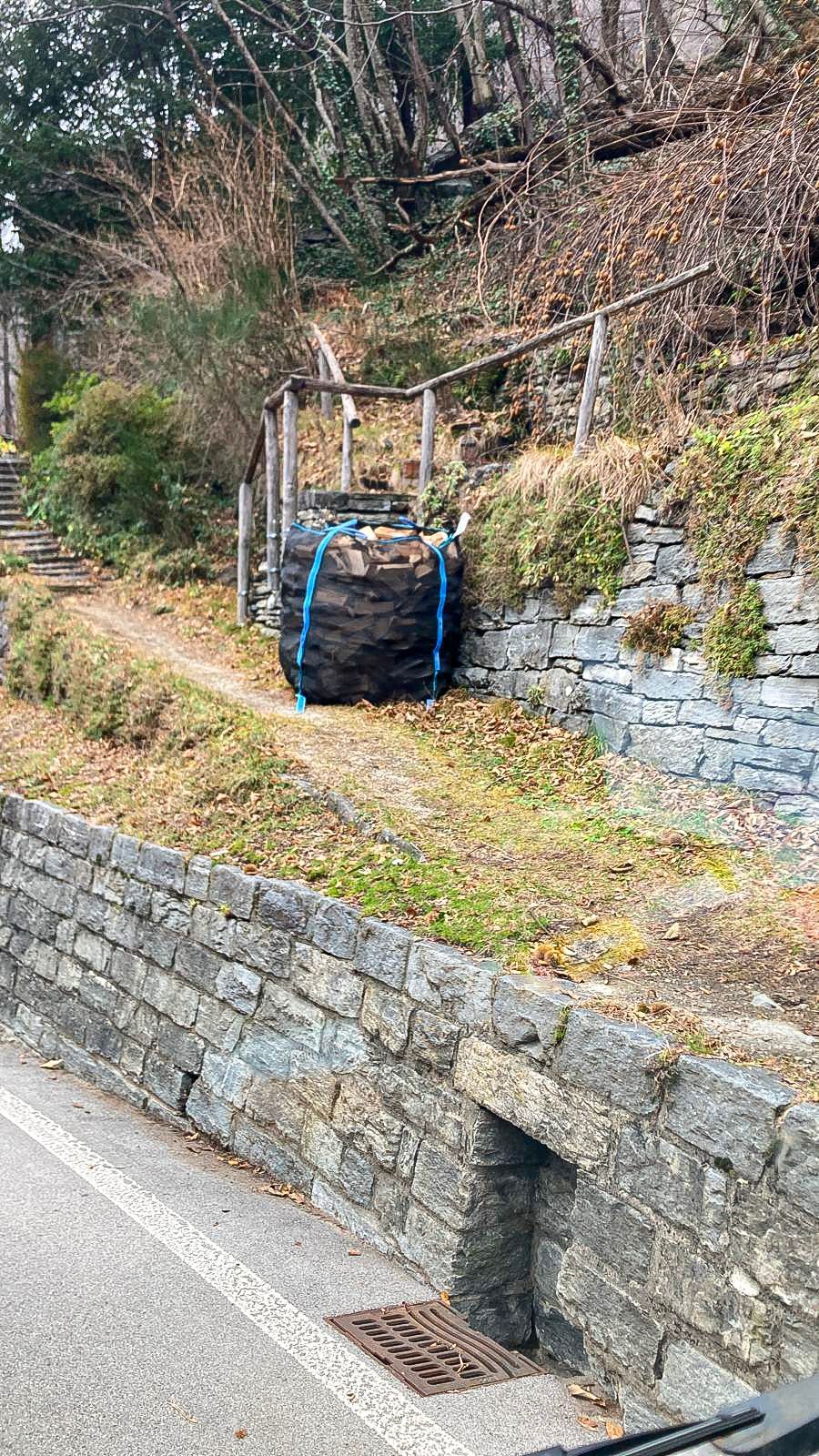 Un sacco di legna è posato sul lato della strada accanto a un muro di pietra.