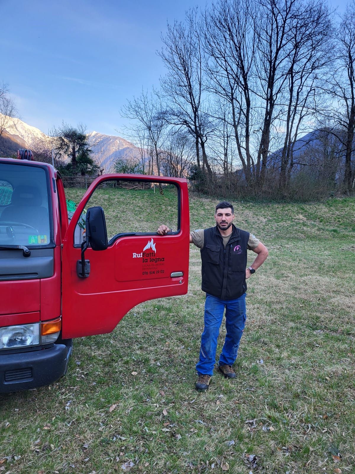 Un uomo è in piedi davanti a un camion rosso in un campo.