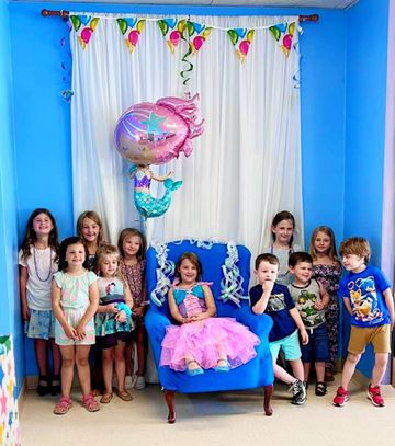 Children posing in a blue party room with balloons and a girl in a pink dress seated on a chair Children posing in a blue party room with balloons and a girl in a pink dress seated on a chair