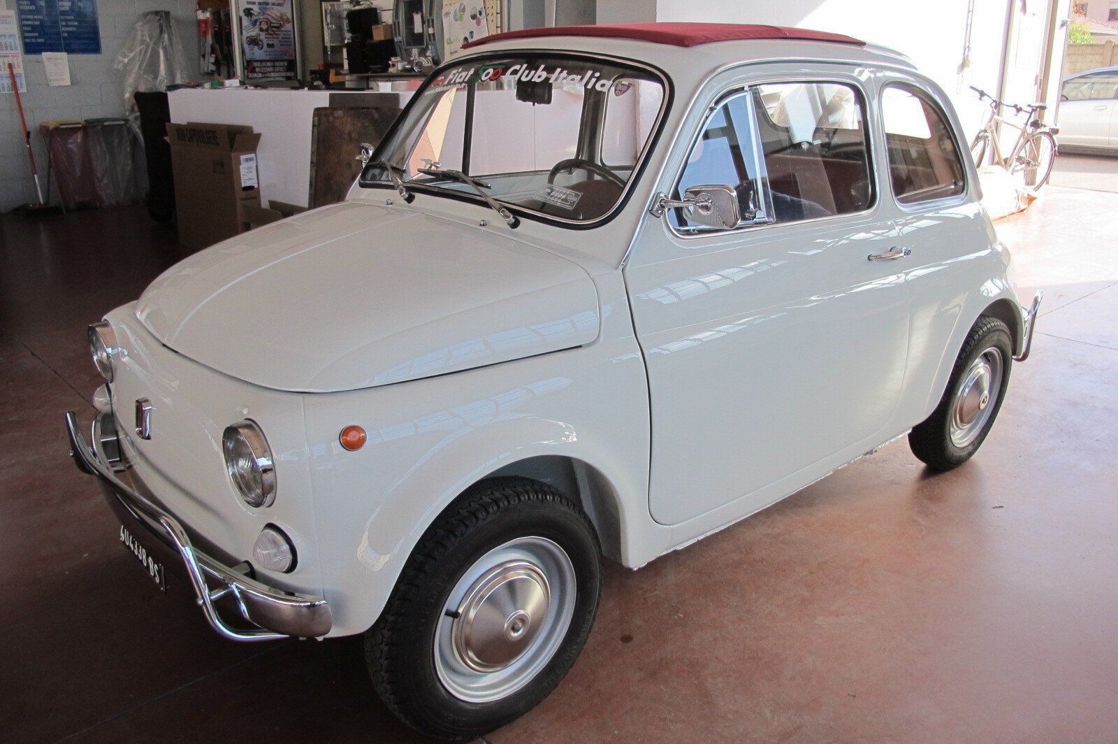 Un'auto d'epoca Fiat 500 bianca con tettuccio apribile rosso, parcheggiata su un pavimento piastrellato.