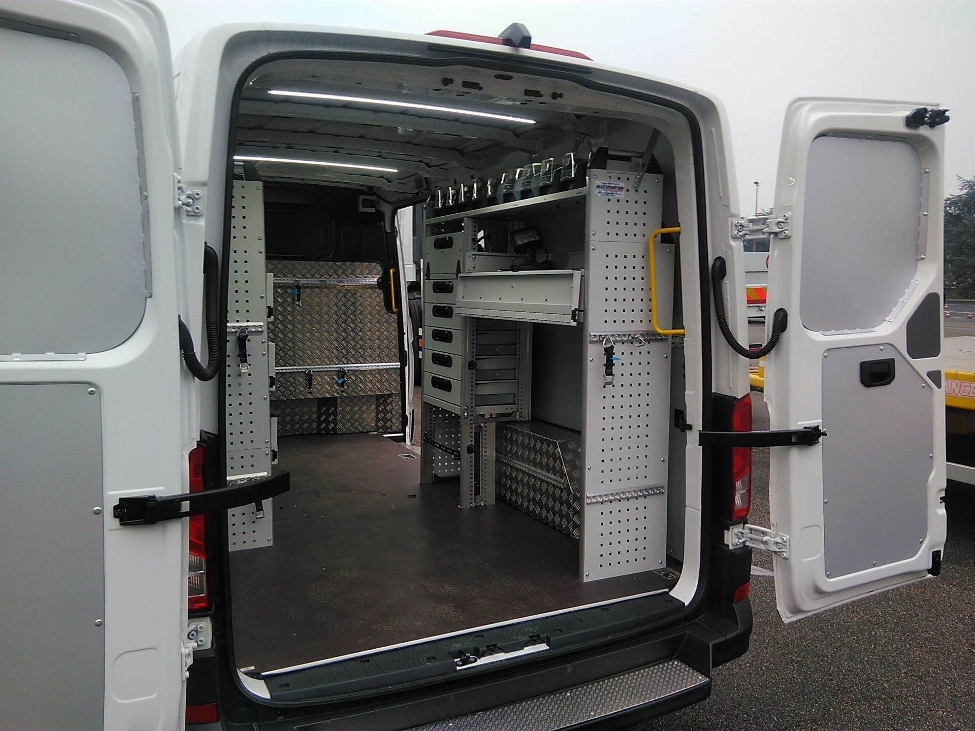 Le porte posteriori aperte di un furgone da lavoro bianco rivelano ripiani e vani portaoggetti organizzati al suo interno.