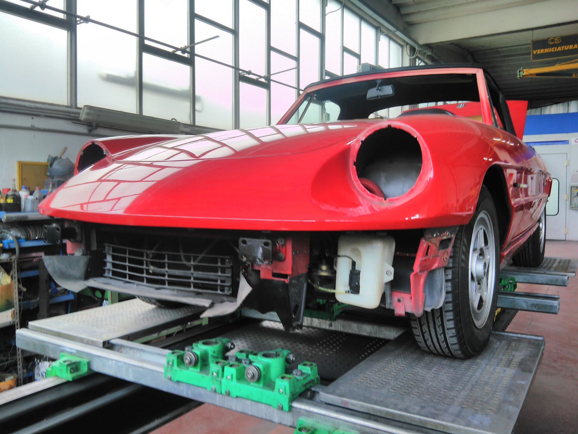 Auto rossa decappottabile su un ponte sollevatore in un'officina, paraurti anteriore rimosso.