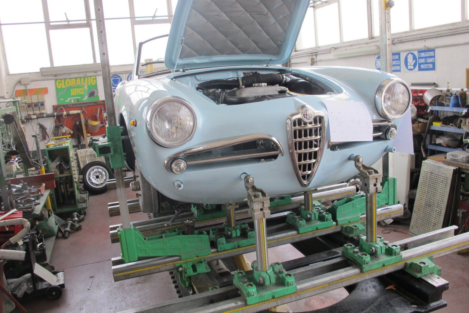 Auto d'epoca azzurra su una macchina per l'allineamento dei telai in un'officina, con il cofano aperto.