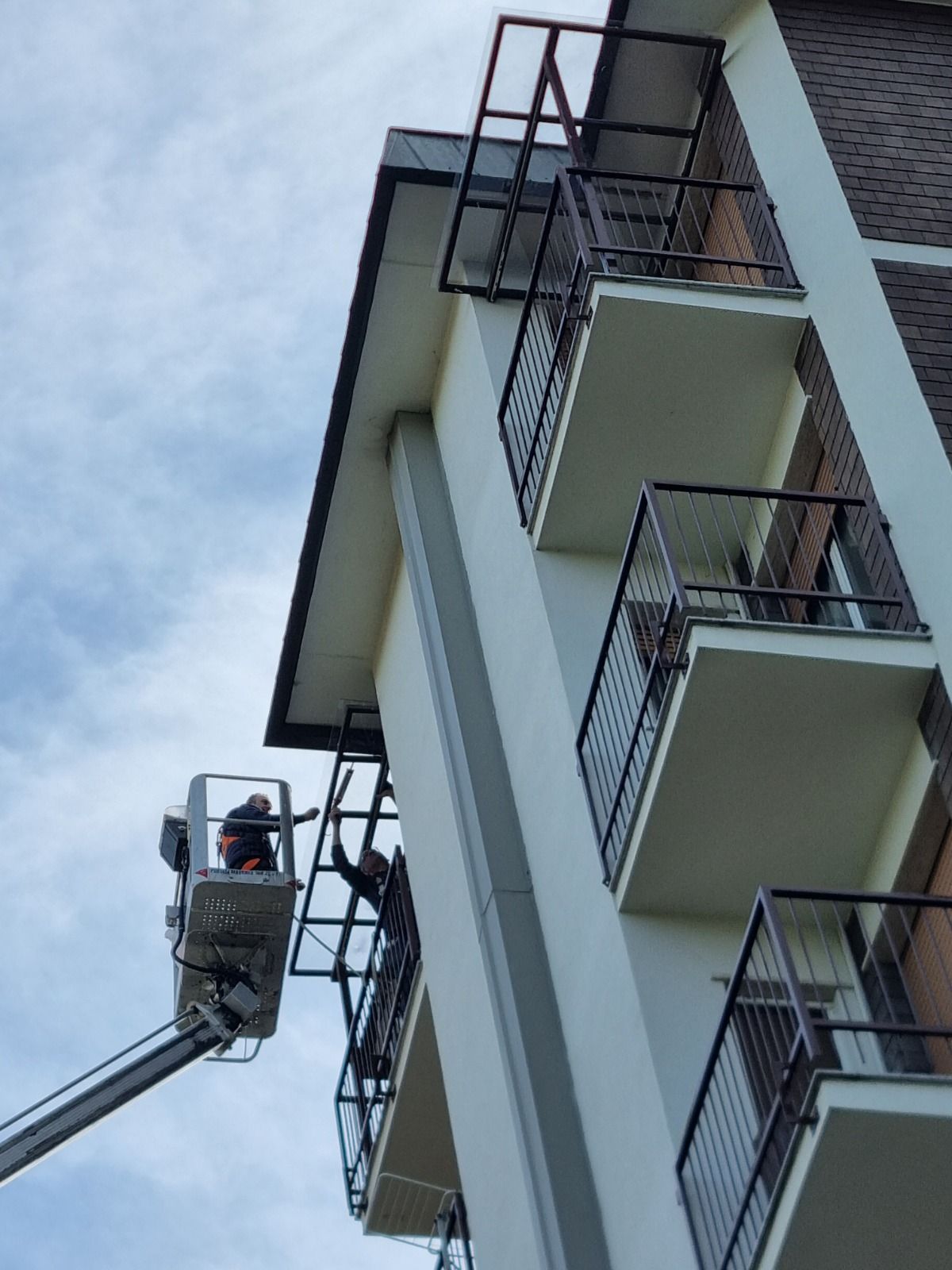 Operai in ascensore lavorano sul tetto di un edificio, installando una struttura metallica vicino ai balconi.
