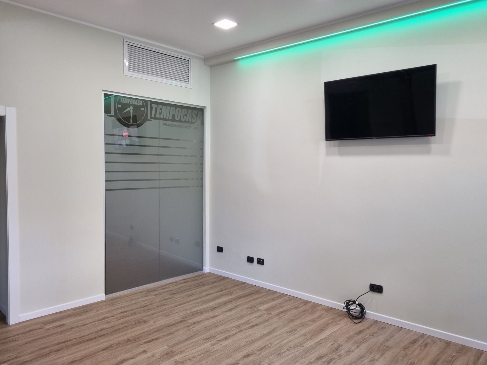 Stanza vuota con una porta a vetri, TV e illuminazione verde dall'alto.