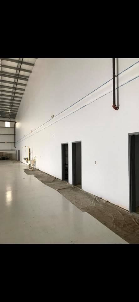 Interior view of a large warehouse with white walls, three doors, and a metal beam ceiling.