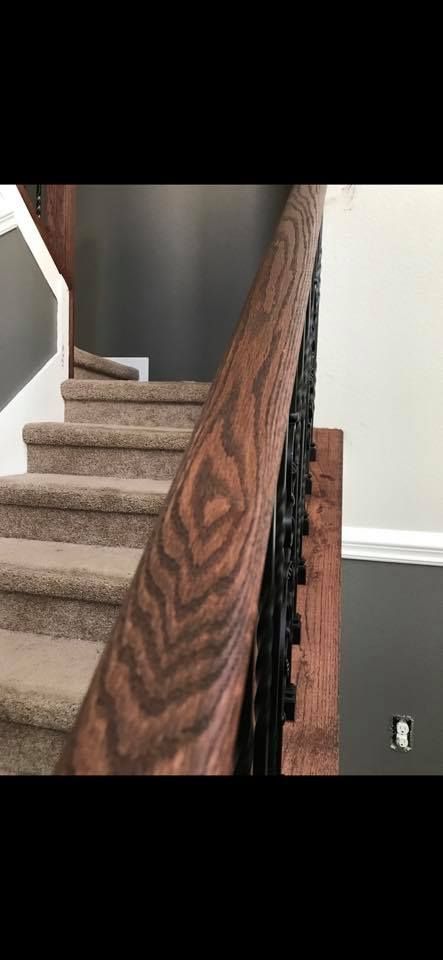 Wooden staircase with carpeted steps and a detailed wood grain handrail. Black spindles, gray and white walls.