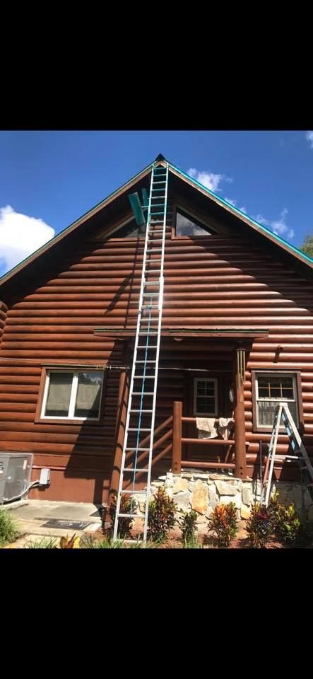 A tall ladder propped against a log cabin for roof access. Blue sky.