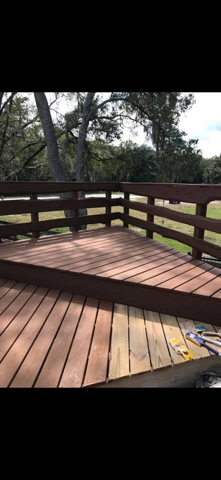Wooden deck with brown railing, in a grassy setting with trees in the background.