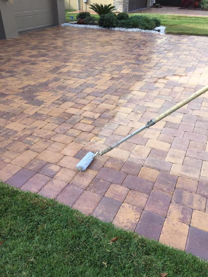 Applying sealant to brick pavers with a roller on a long handle; the pavers are brown and red.